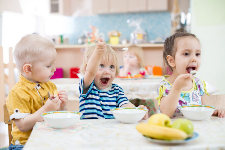 Happy little boy excitedly holding up his fork while eating at nursery