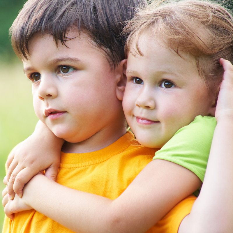 Little boy staring into the distance in a field with a younger girl hugging him from behind