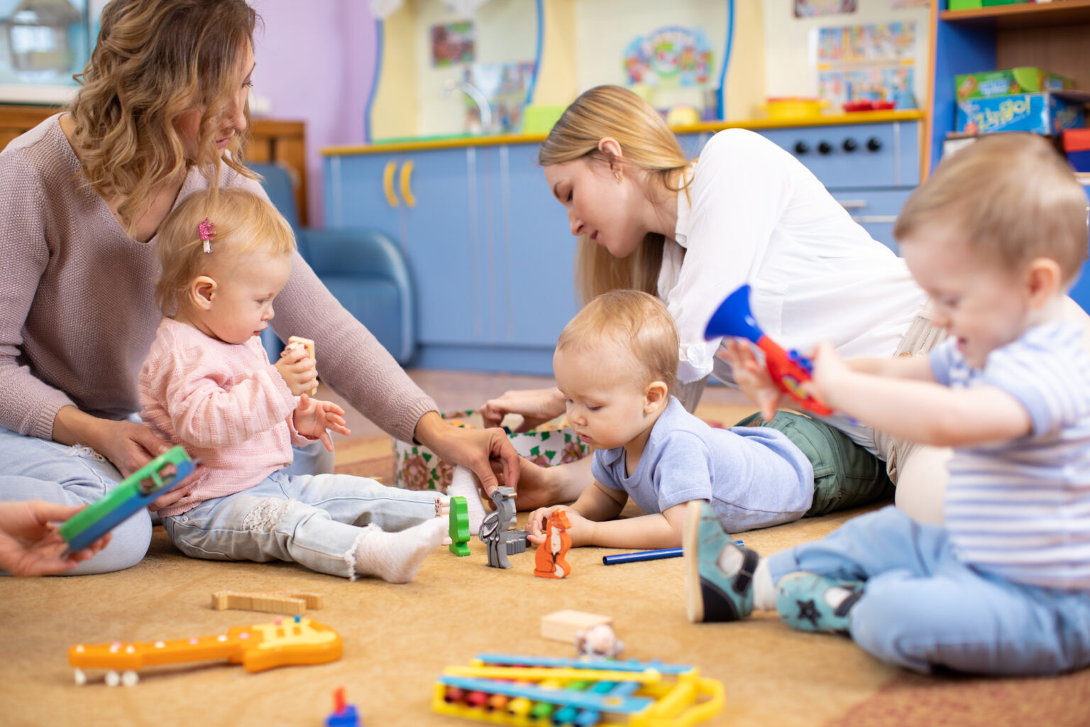 Group of mothers with children playing on the floor with toys
