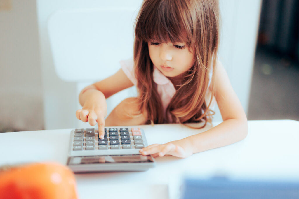 Little girl sat at a table entering numbers into a calculator