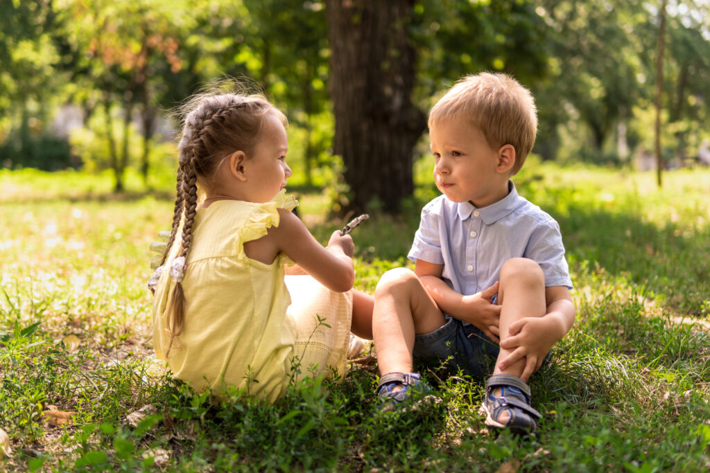 Toddler girl and boy sat outside on the grass talking to each other