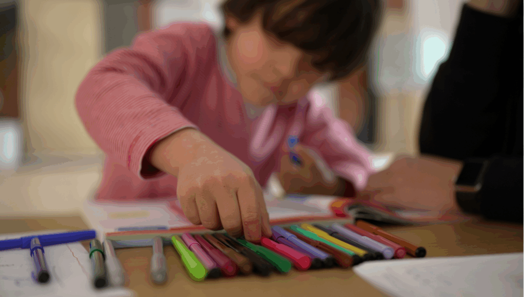 Little boy reaching into a selection of colourful pens lined up on the table