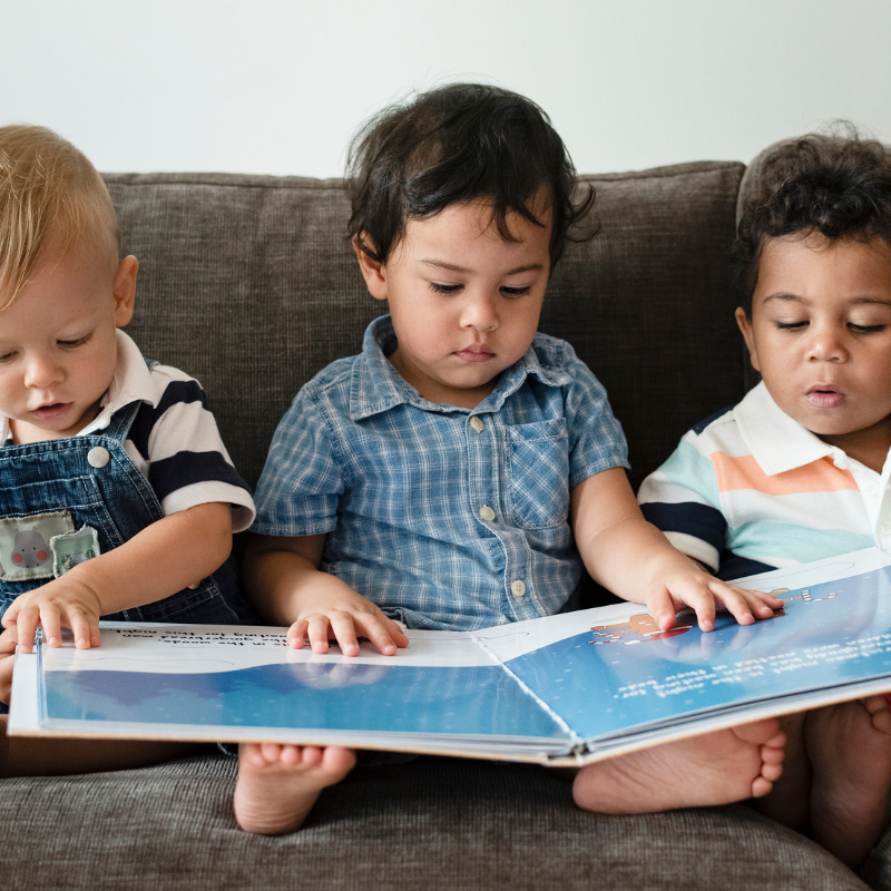 Three little boys reading a book on a sofa