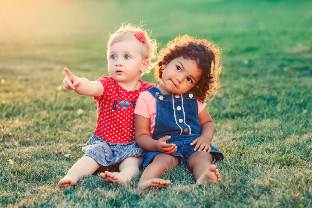 Two toddlers sat side by side on the grass