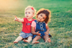 Two toddlers sat side by side on the grass