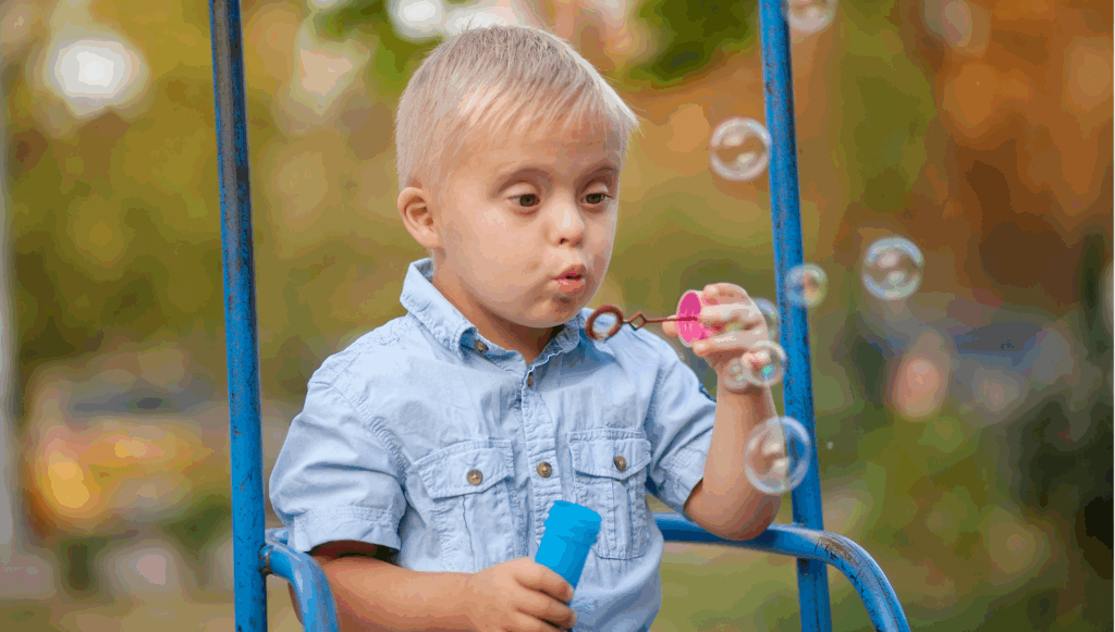 Little hoy with Down Syndrome sat on a swing blowing bubbles