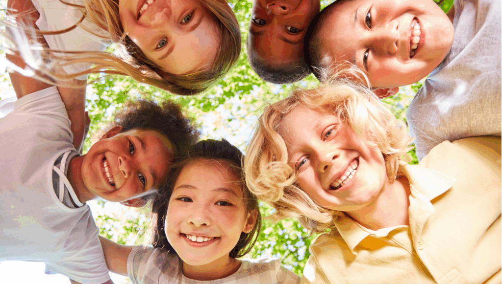 Group of children of different races gathered around each other looking down at the camera