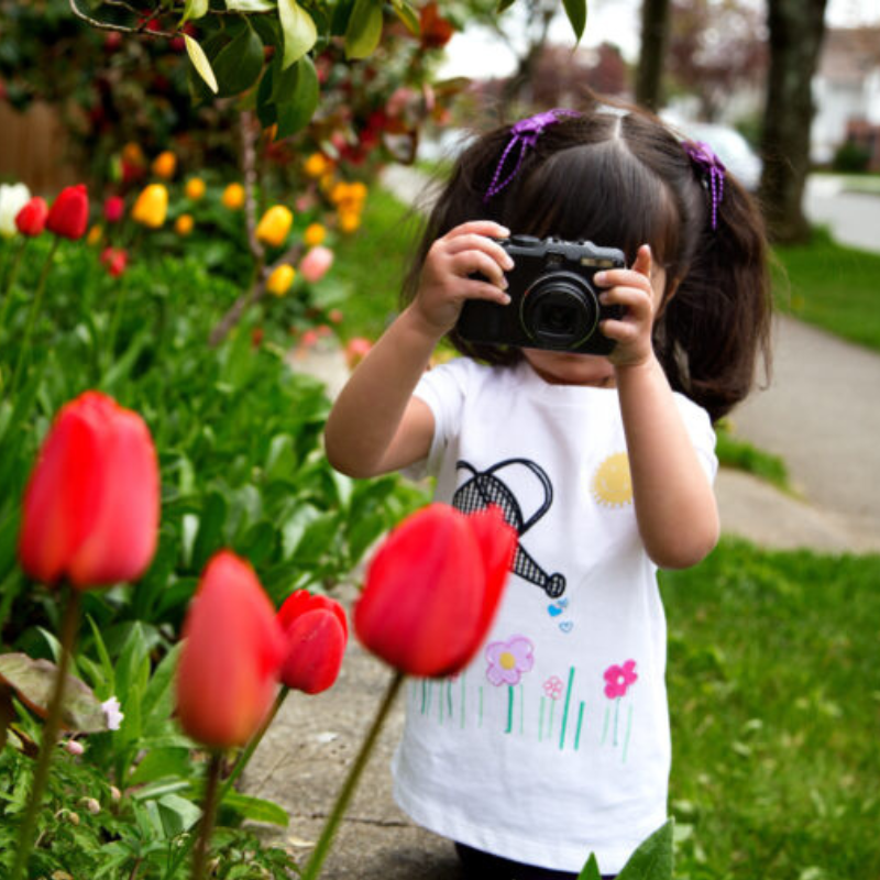 Young girl looking through viewfinder of her camera making a photo of spring flowers