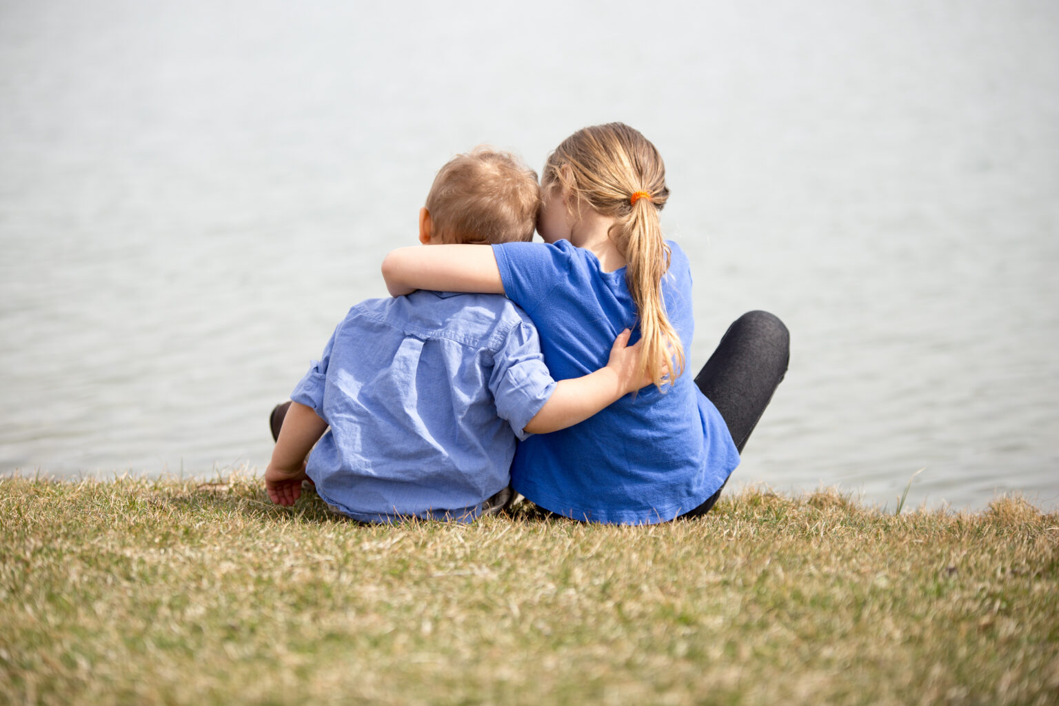Girl sat next to boy hugging around his shoulders looking out into the sea
