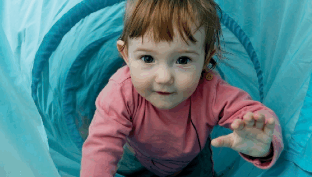 Little girl crawling through a blue toy tunnel towards the camera