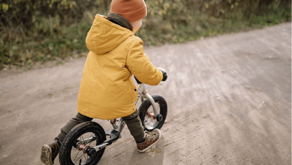 Child in a yellow coat and winter hat riding a bike