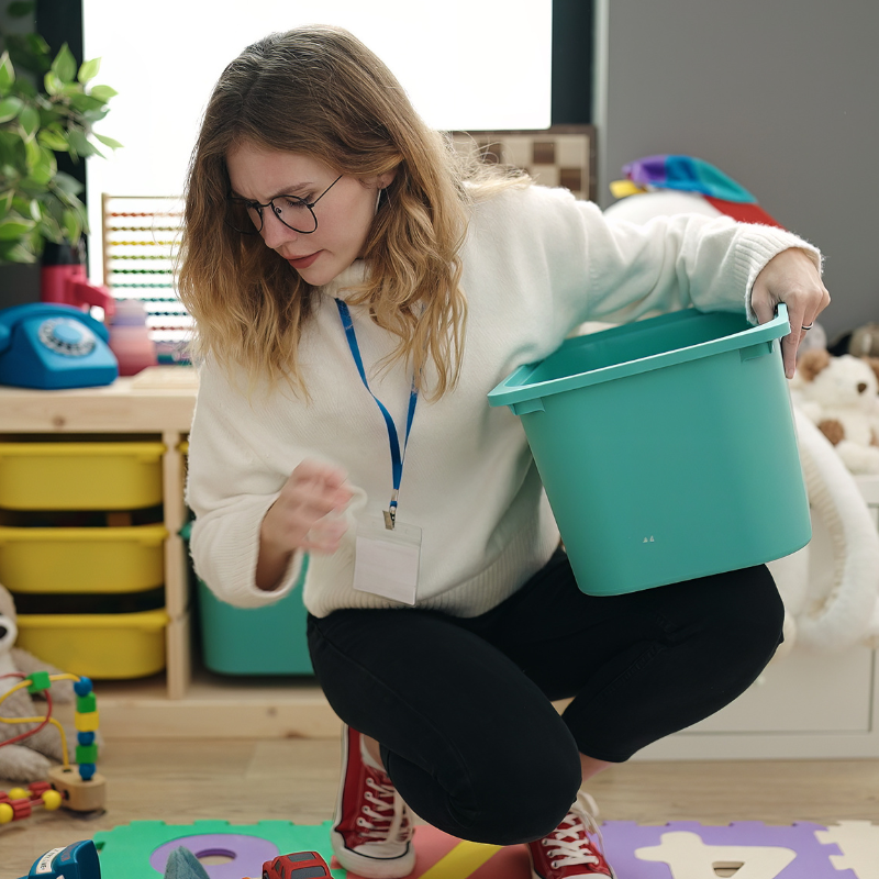 Preschool teacher picking up toys at kindergarten