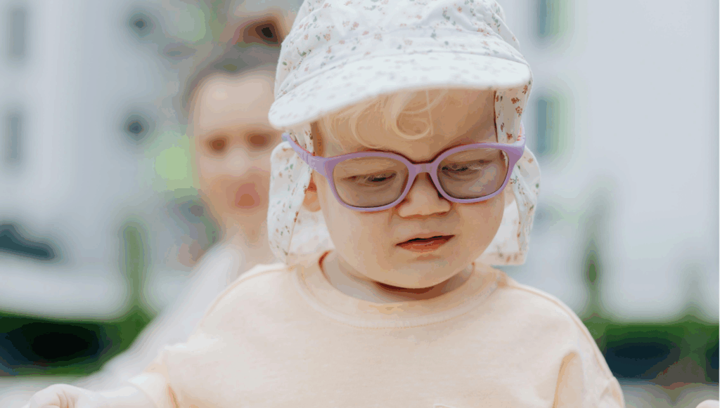 Little girl wearing a light pink top, a white sun hat and glasses