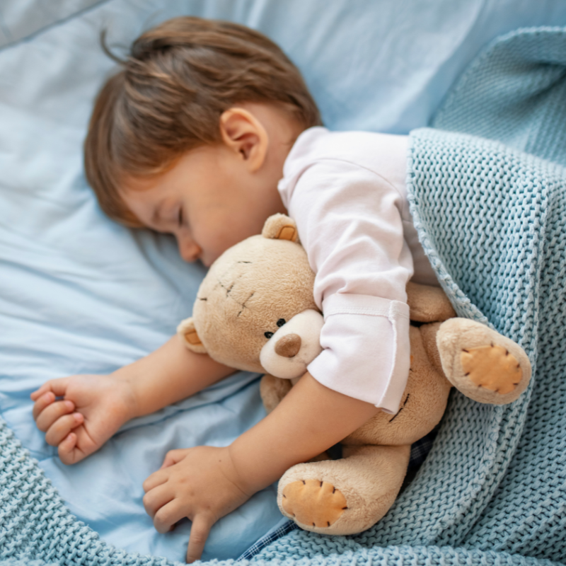Little boy asleep in bed cuddling a teddy bear