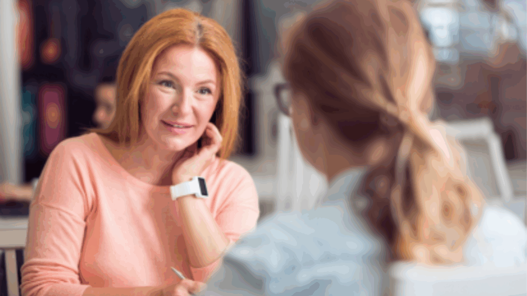 Woman with red hair sat opposite a woman in a blue short at an interview