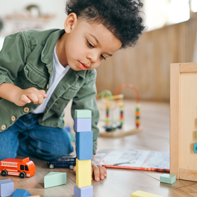 Little boy carefully building a stack of colourful building blocks