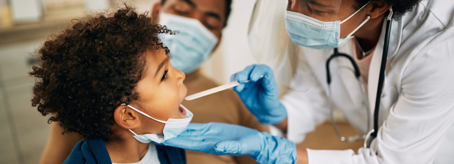 Family doctor examining throat of a small boy while visiting him at home