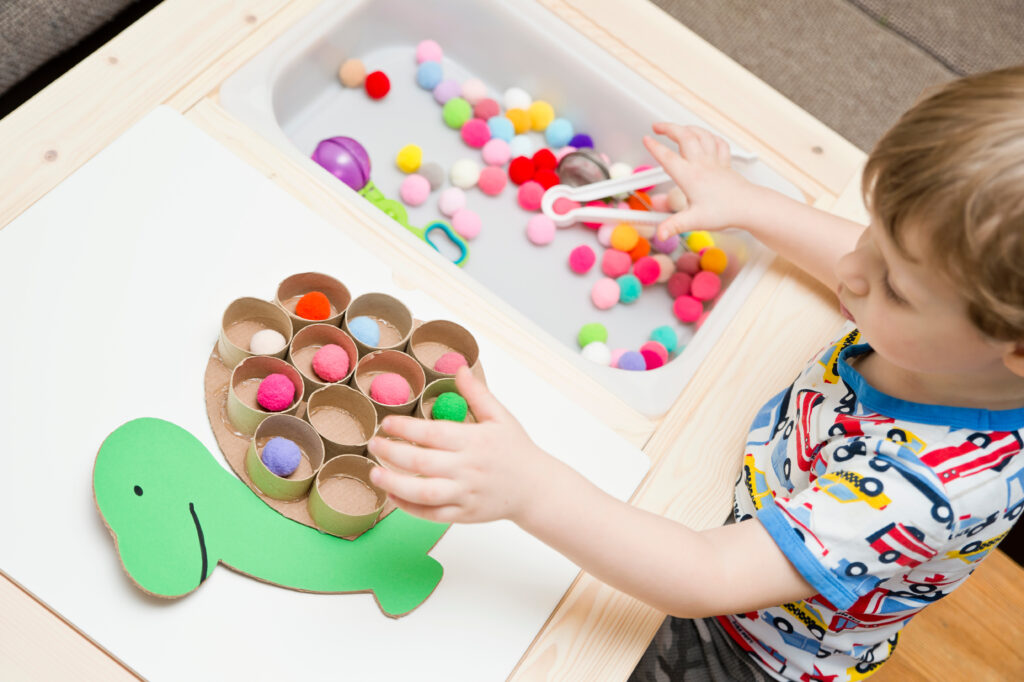 Child sorting colourful pom poms into a homemade cardboard turtle