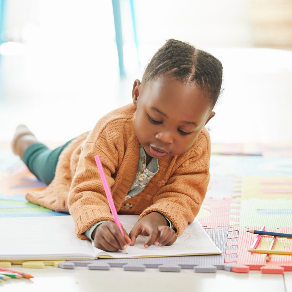 Little girl lying on the floor writing with a pink pencil