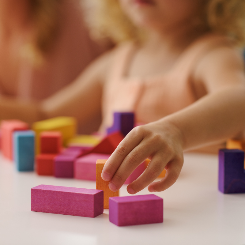 Little girl's hand reaching for colourful wooden blocks
