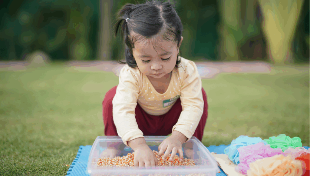 Little girls playing with sensory tray outdoors on grass