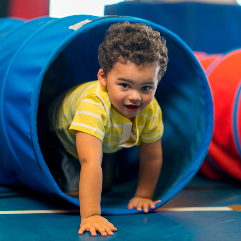 Little boy in yellow t-shirt climbing through a toy tunnel