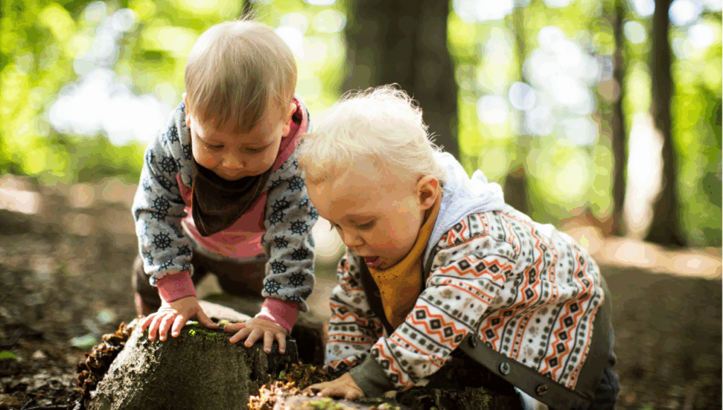 Two toddler leaning on a tree stump in the woods