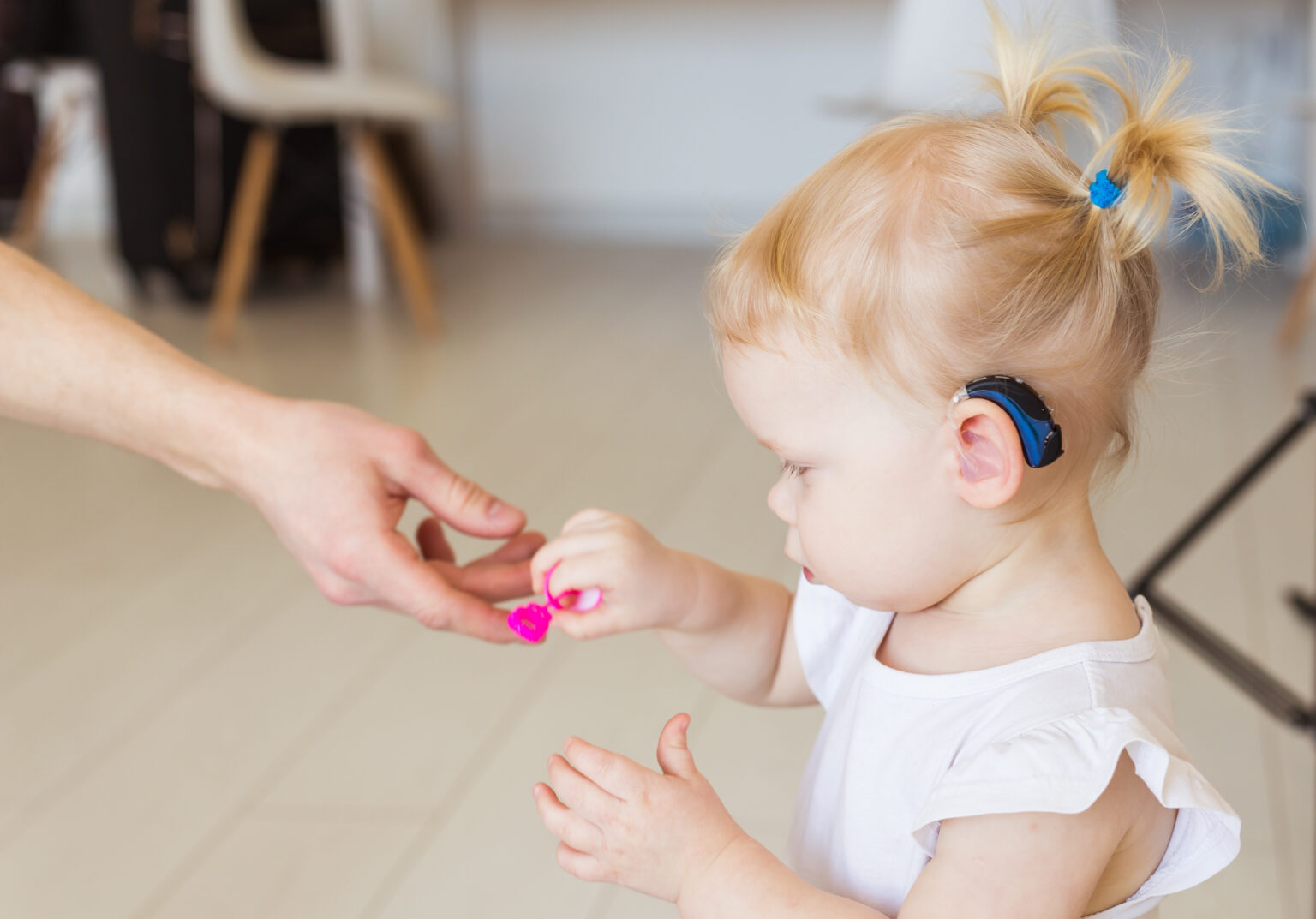 Little girl wearing a hearing aid being handed a toy