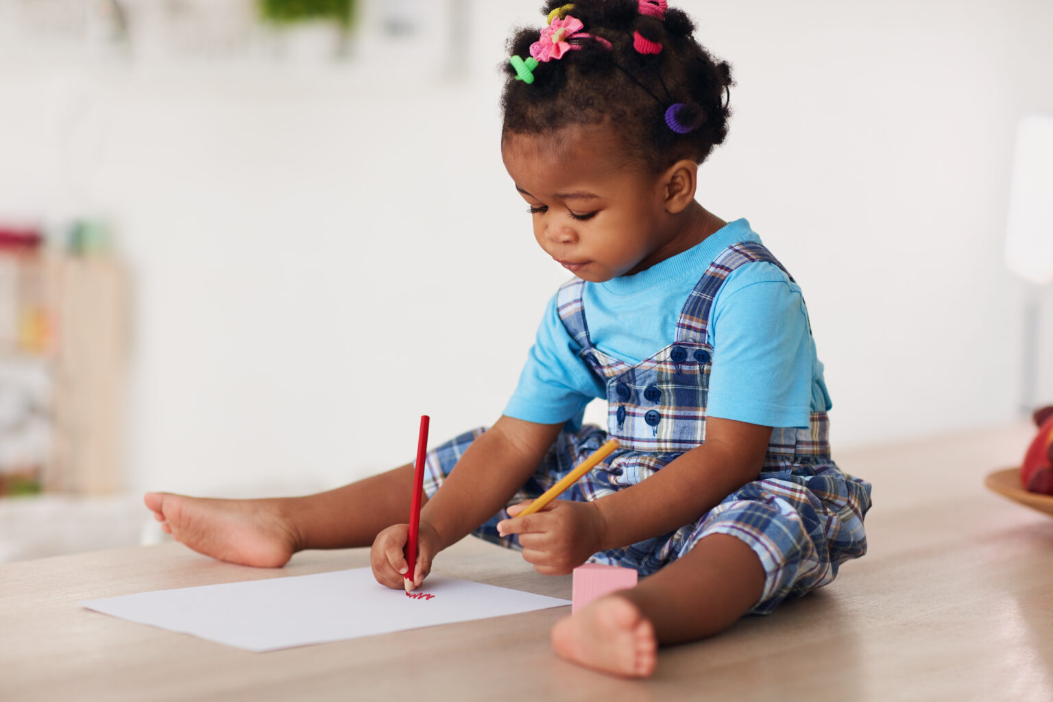 Toddler girl sat on the floor drawing with pencils using both hands