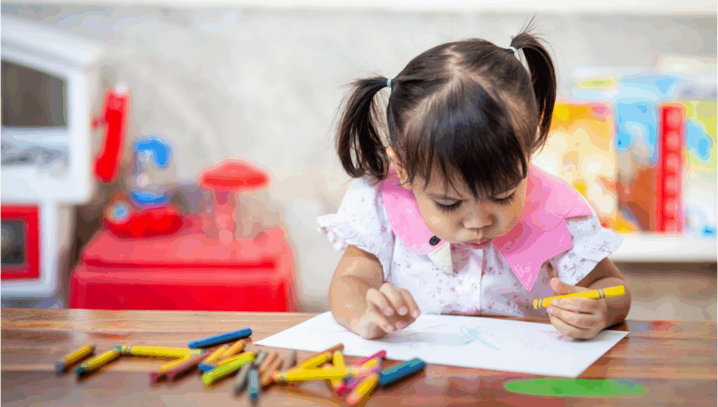 Little girl with pigtails drawing on a blank piece of paper with colourful crayons