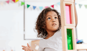 Little girl stacking colourful wooden building blocks above her head
