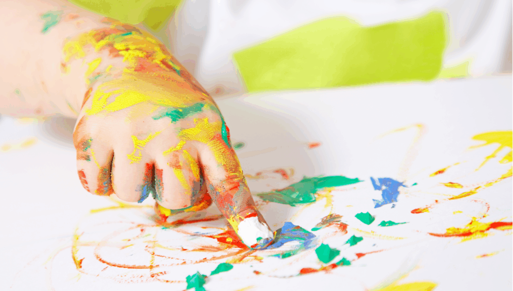 Close-up of a child finger covered in colourful paints fingerpainting on a white piece of paper