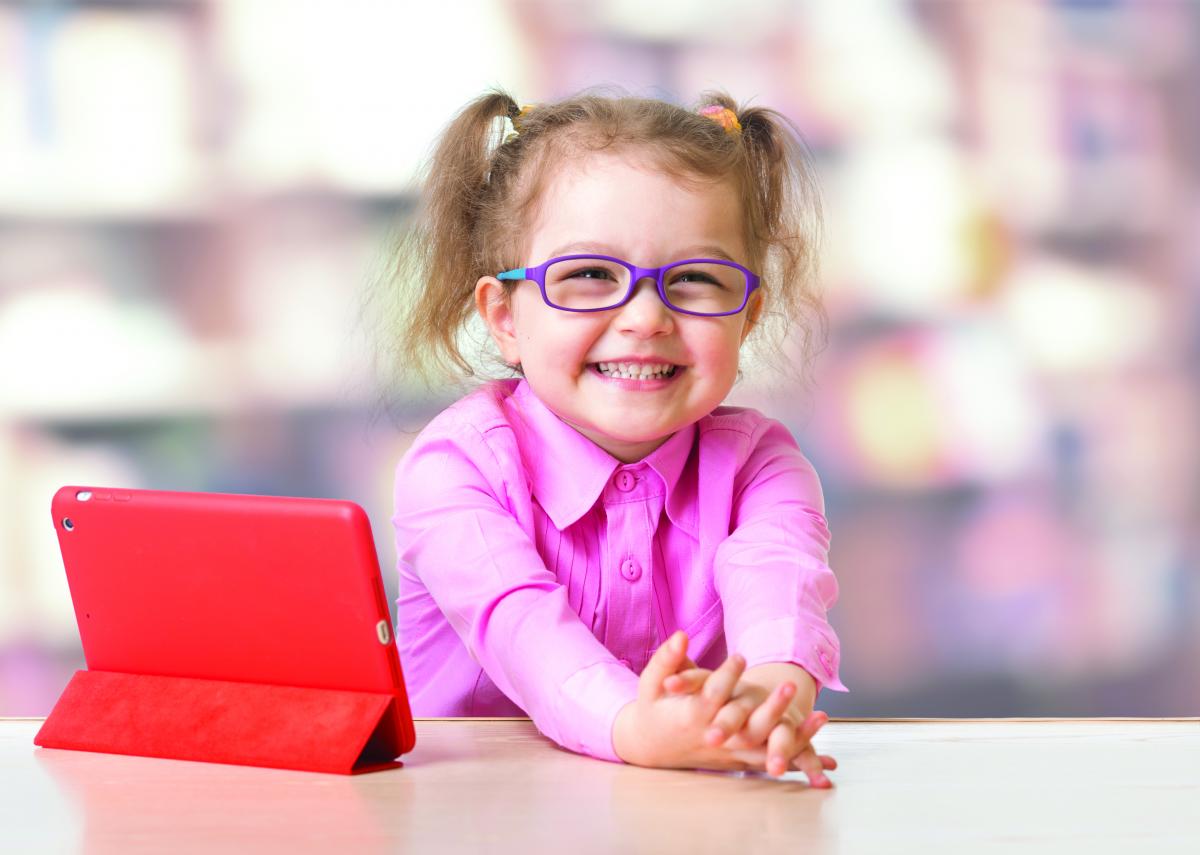a young girl beams, tablet computer on the table next to her