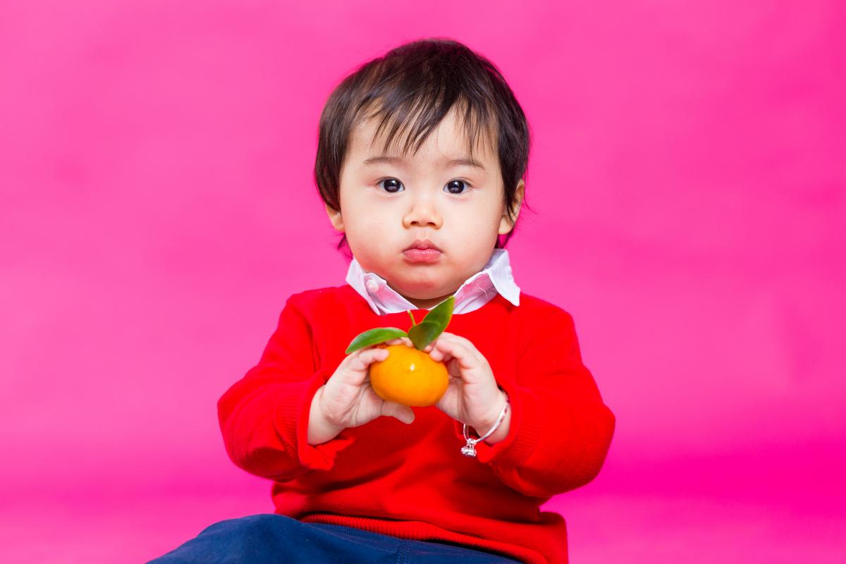a little boy holds a mandarin - considered good fortune in Chinese culture