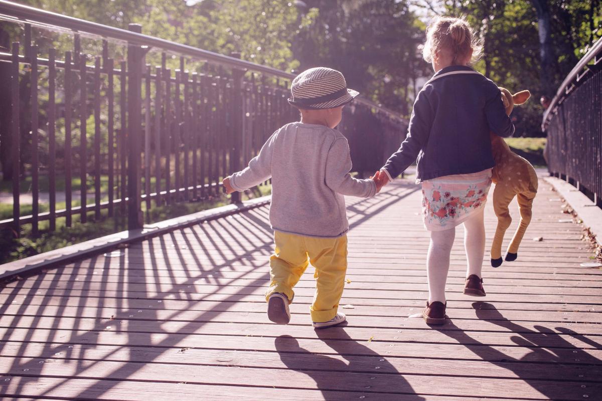 a boy and girl hold hands as they walk across a bridge
