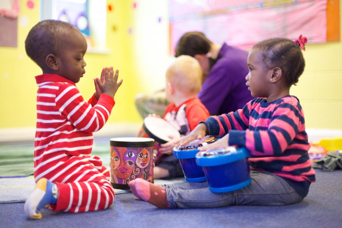 A young girl plays bongos whilst a young boy claps along