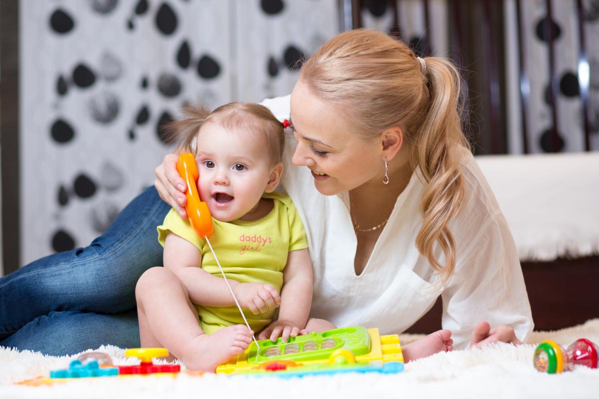 a mother plays with toddler and toy phone