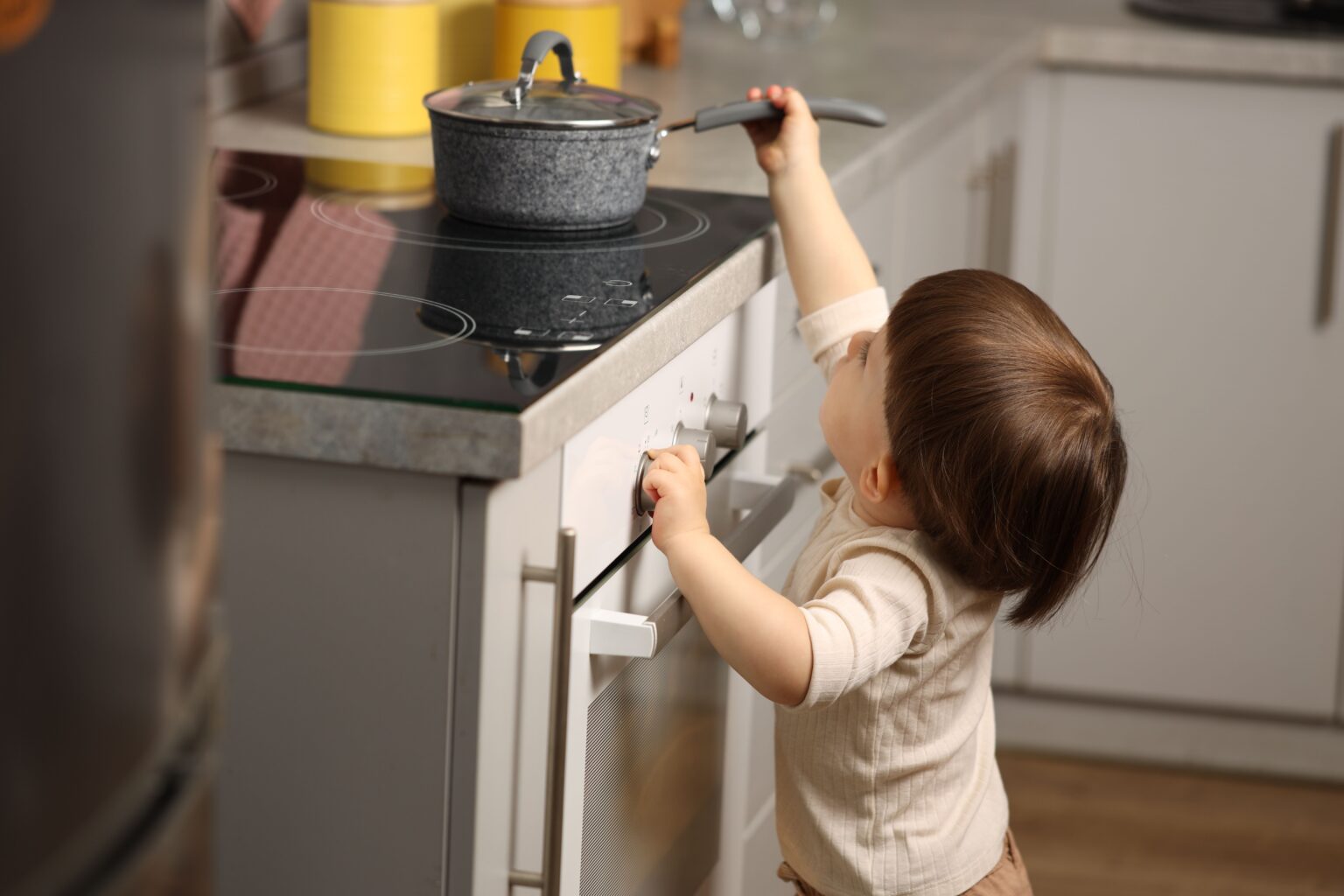 Little boy playing with pot on stove in kitchen.