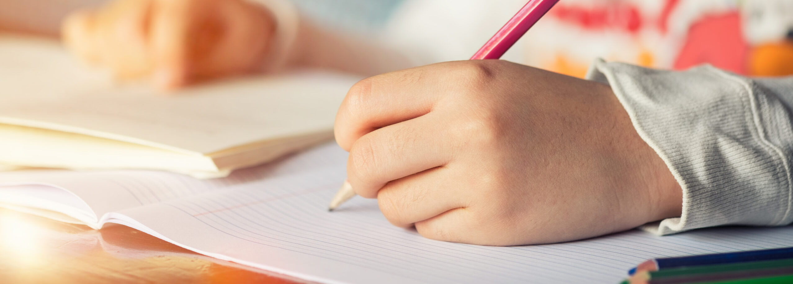 Close-up of a child's hand writing in a notepad with a red pencil