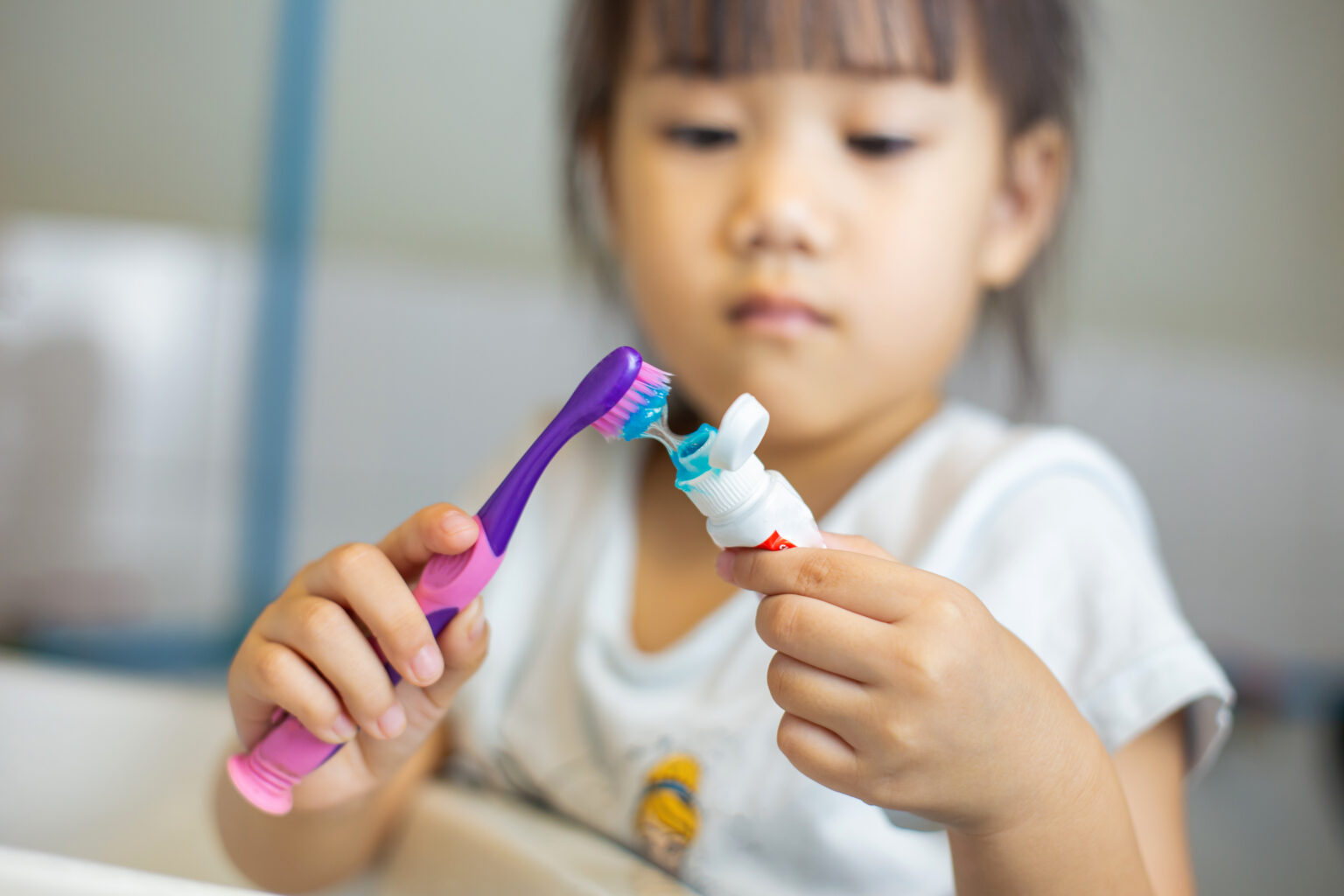 Little girl holding a purple toothbrush squeezing toothpaste onto it