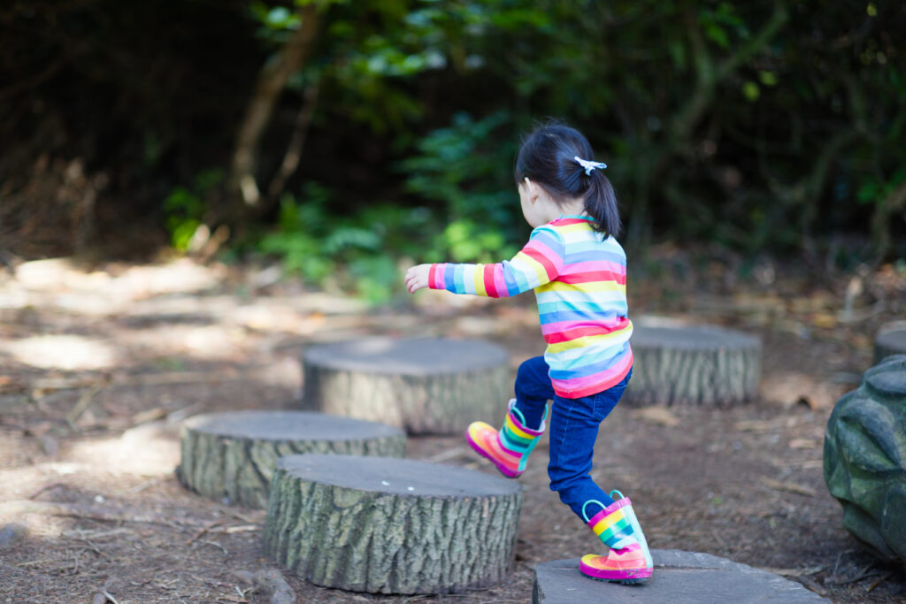 young girl jumping between the timber in the forest park