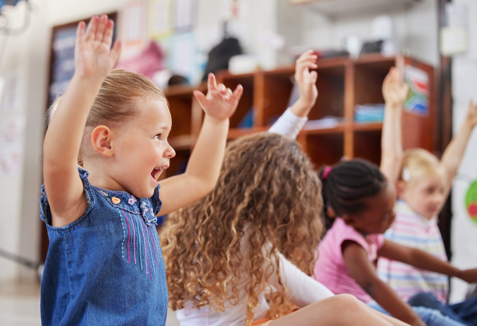 Group of excited children sitting side by side with their hands in the air
