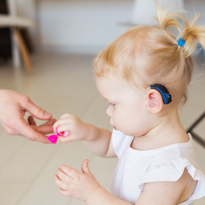 Little girl wearing a hearing aid being handed a toy
