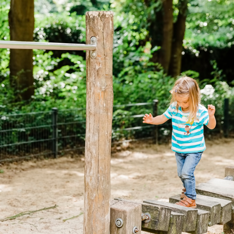 Toddler girl balancing while walking on wooden playground equipment