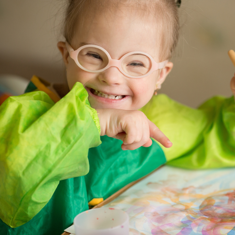 Little girl in glasses smiling, covered in paint when drawing