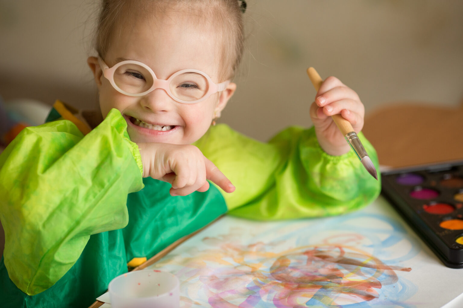 Little girl in glasses smiling, covered in paint when drawing