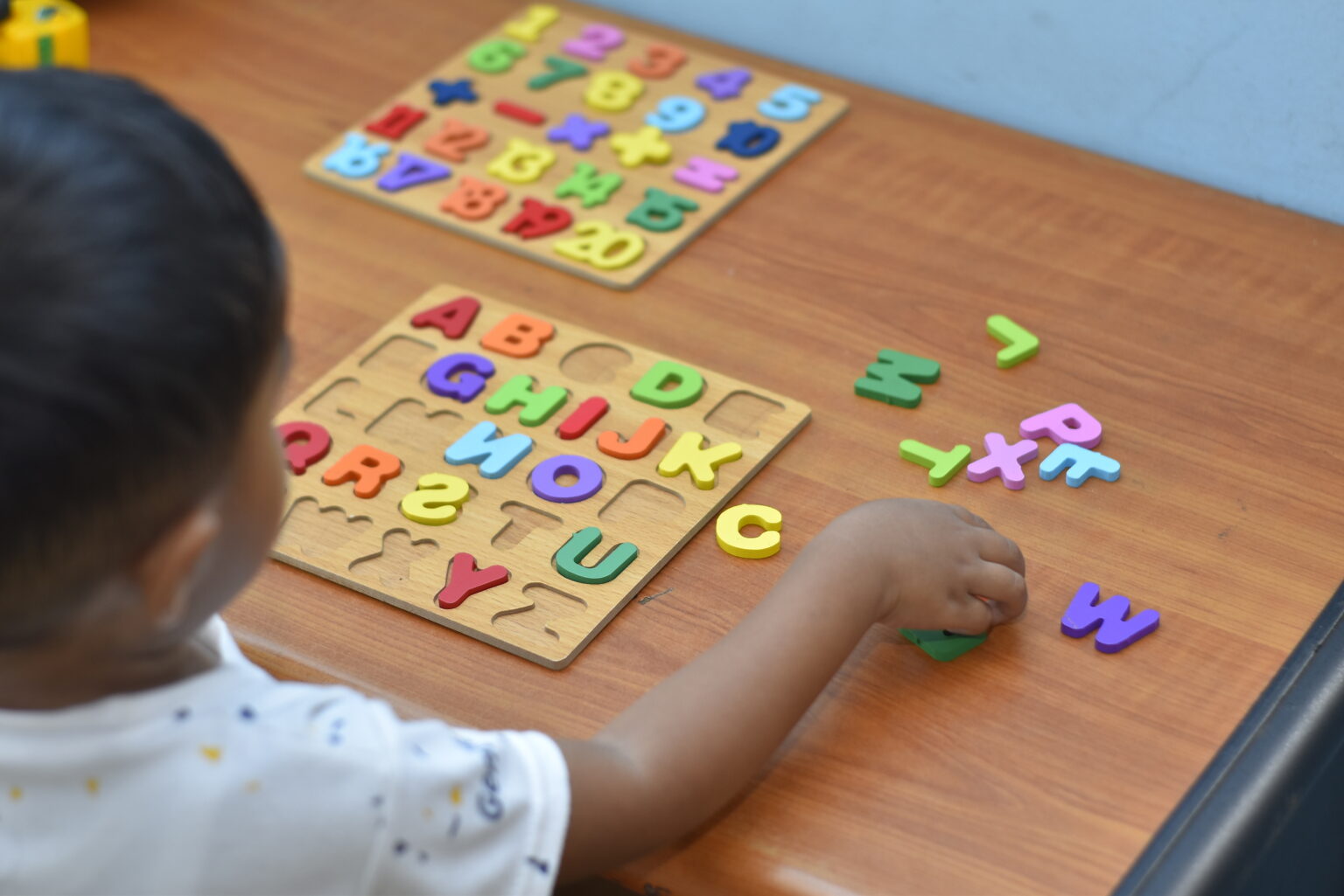 Little boy facing away from the camera playing with a wooden letter sorting today