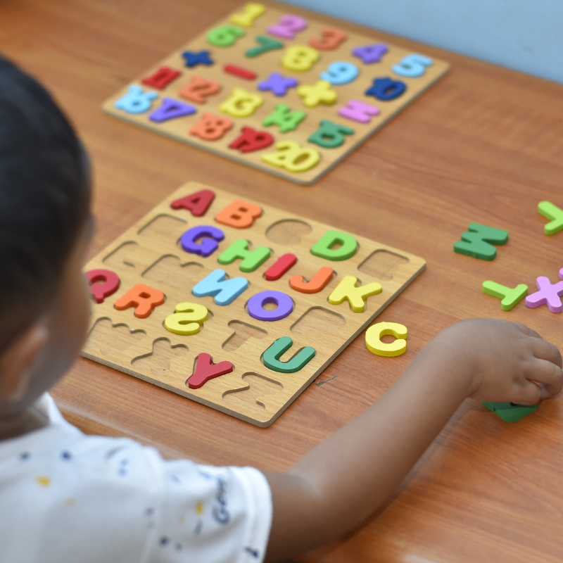 Little boy facing away from the camera playing with a wooden letter sorting today