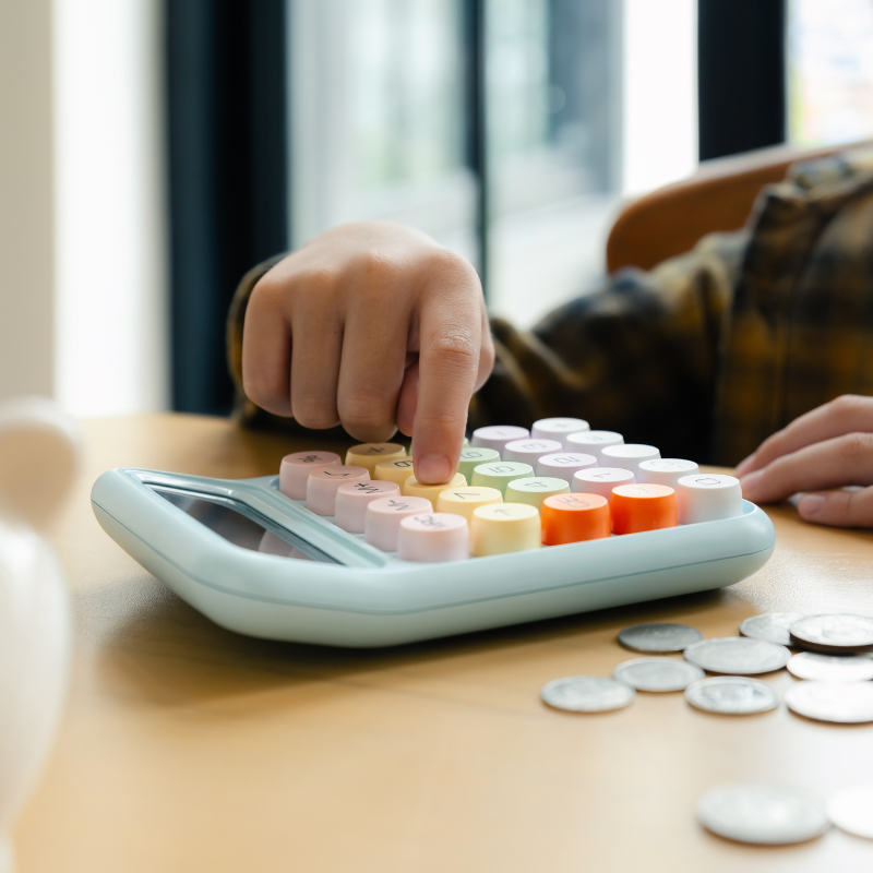 Child tapping a calculator with coin next to it on a desk