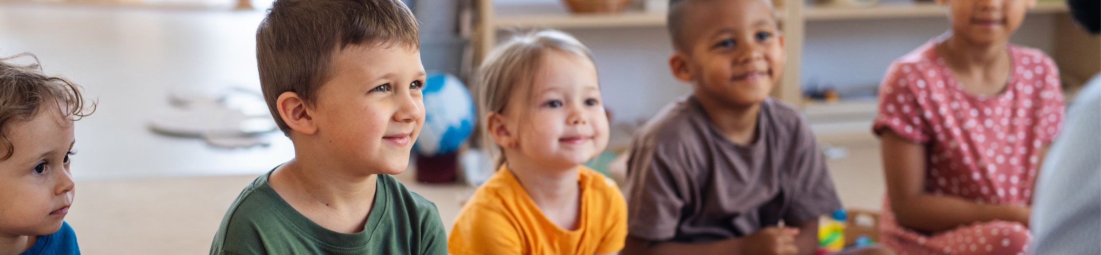 Group of pre-school child sat on the floor smiling at someone off camera